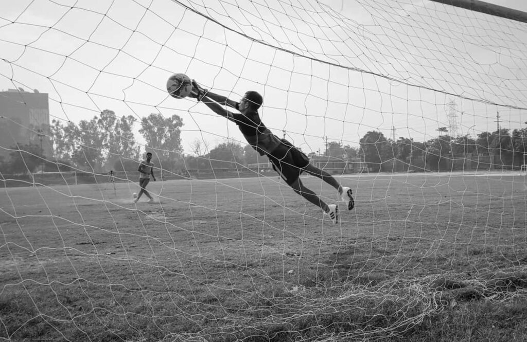A goalkeeper makes an impressive dive to save a soccer ball during a match.